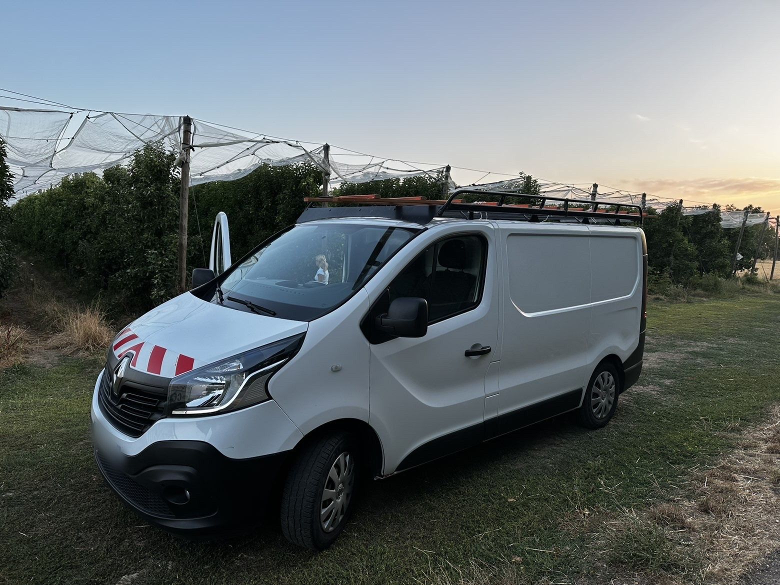 Camion utilitaire blanc de Melis Habitat avec galerie de toit, garé au coucher du soleil